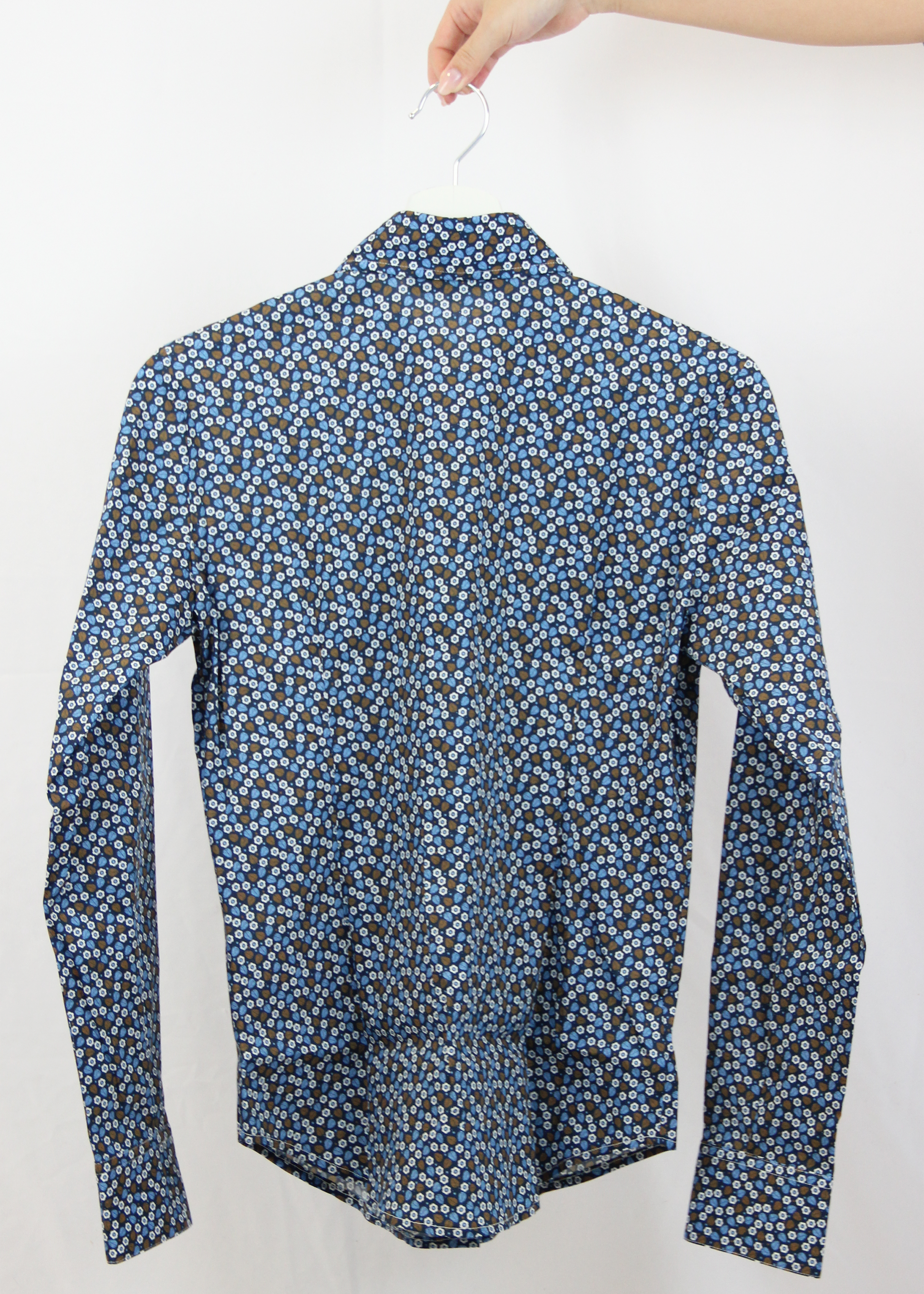 Camicia da donna in cotone con fantasia floreale su sfondo blu. Il design elegante presenta un pattern delicato di piccoli fiori e foglie nei toni dell’azzurro e del marrone, ideale per un look raffinato e senza tempo. Realizzata artigianalmente dalla maglieria Strike Inside Abbigliamento a Genova, questa camicia unisce qualità sartoriale e comfort, perfetta per ogni occasione.