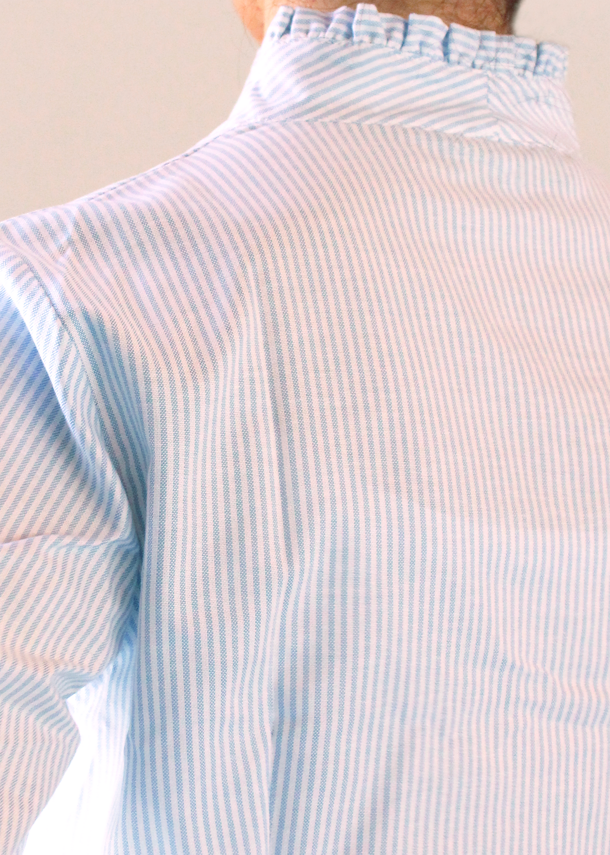 Camicia artigianale a righe fini azzurre e bianche in 100% cotone. Design elegante con scollo a V e rouches femminili. Realizzata dalla maglieria artigianale di Genova di Strike Inside. Made in Italy.