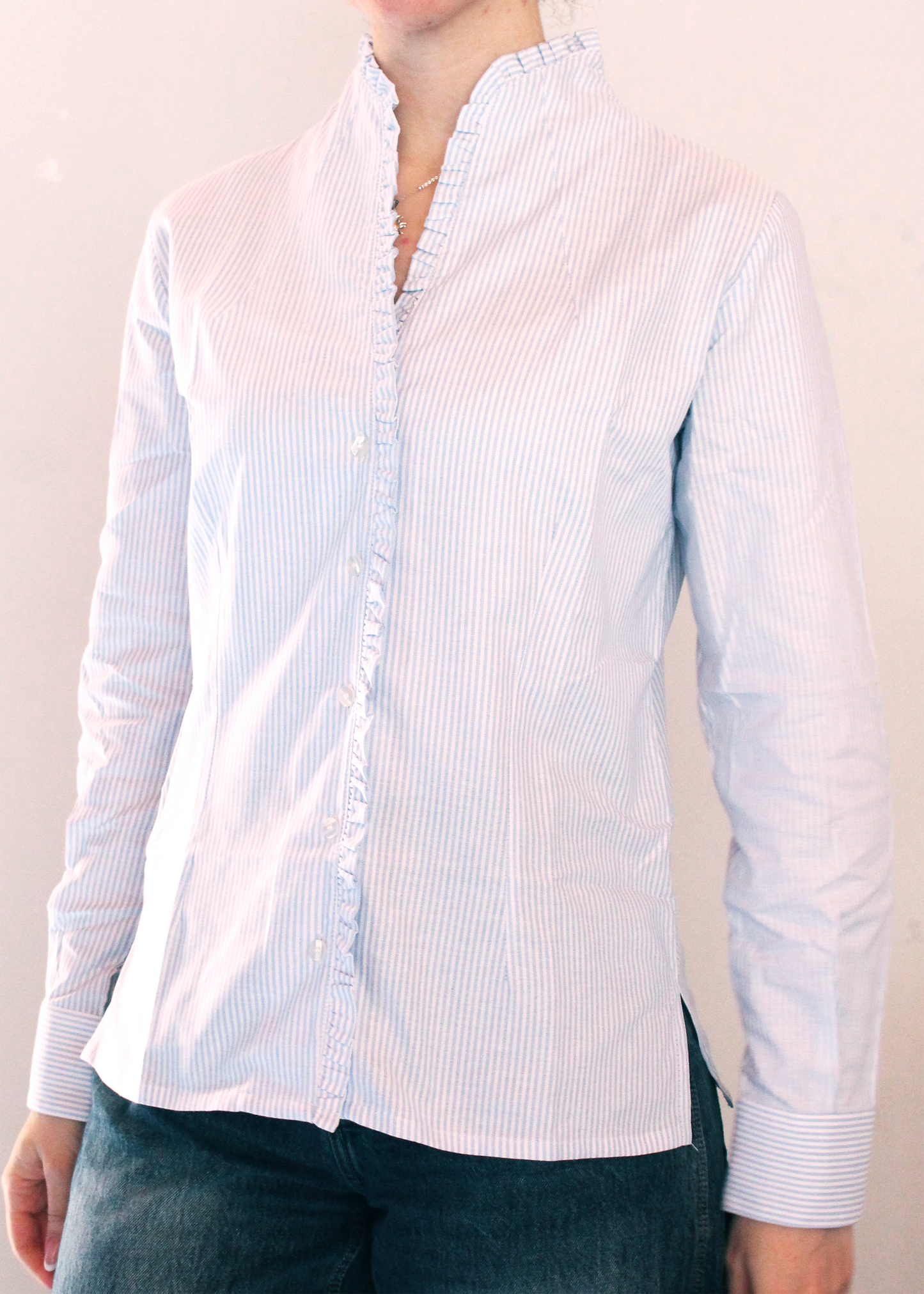 Camicia artigianale a righe fini azzurre e bianche in 100% cotone. Design elegante con scollo a V e rouches femminili. Realizzata dalla maglieria artigianale di Genova di Strike Inside. Made in Italy.