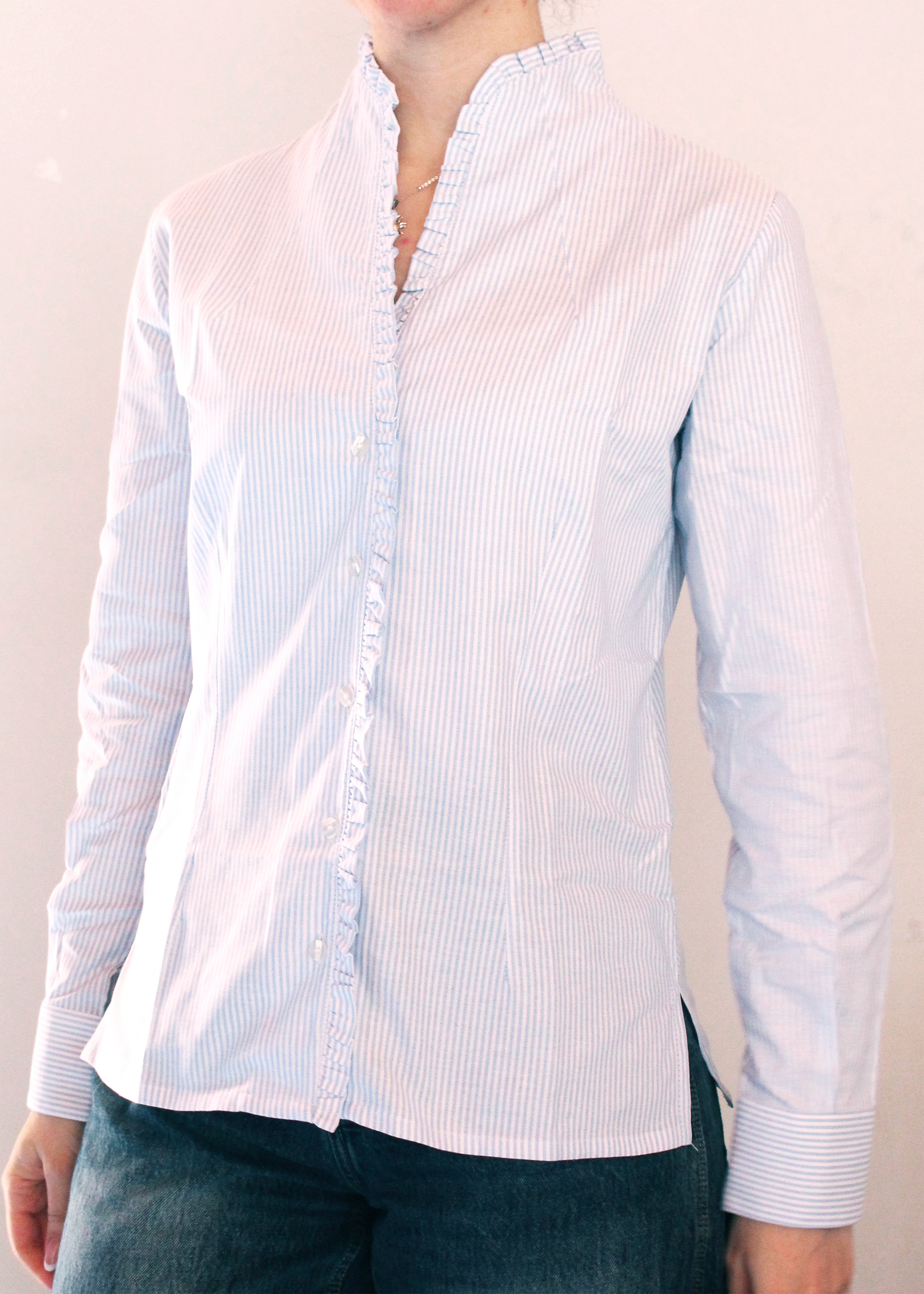 Camicia artigianale a righe fini azzurre e bianche in 100% cotone. Design elegante con scollo a V e rouches femminili. Realizzata dalla maglieria artigianale di Genova di Strike Inside. Made in Italy.