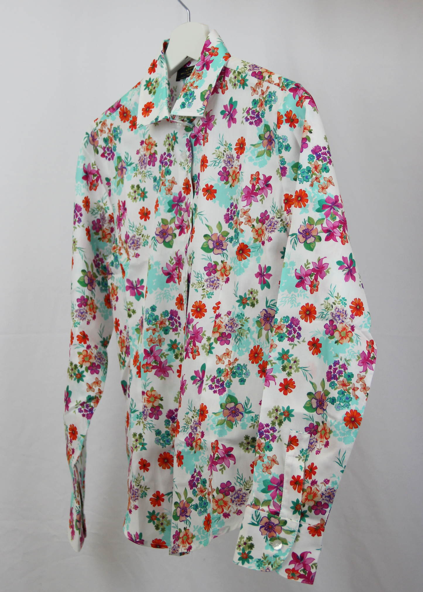 Camicia da donna in cotone dal taglio classico, realizzata artigianalmente da Strike Inside. Il tessuto leggero e traspirante presenta una vivace fantasia floreale su sfondo bianco, decorato con fiori multicolore nei toni del rosso, fucsia, verde e viola. Il design con colletto tradizionale e chiusura con bottoni la rende un capo versatile, perfetto per un look fresco e raffinato. Un'elegante espressione di artigianalità e stile, ideale per aggiungere un tocco di colore al guardaroba.