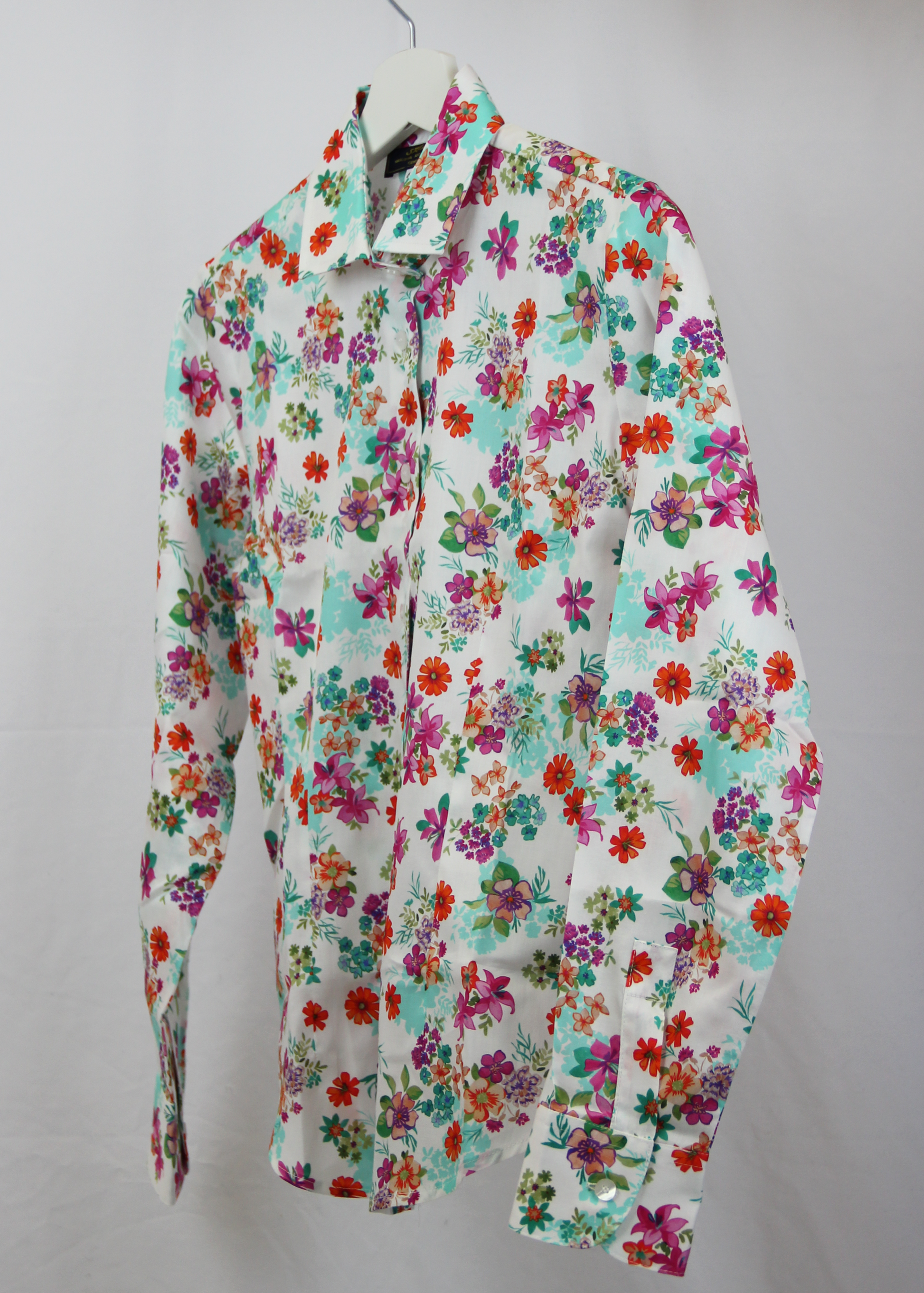 Camicia da donna in cotone dal taglio classico, realizzata artigianalmente da Strike Inside. Il tessuto leggero e traspirante presenta una vivace fantasia floreale su sfondo bianco, decorato con fiori multicolore nei toni del rosso, fucsia, verde e viola. Il design con colletto tradizionale e chiusura con bottoni la rende un capo versatile, perfetto per un look fresco e raffinato. Un'elegante espressione di artigianalità e stile, ideale per aggiungere un tocco di colore al guardaroba.