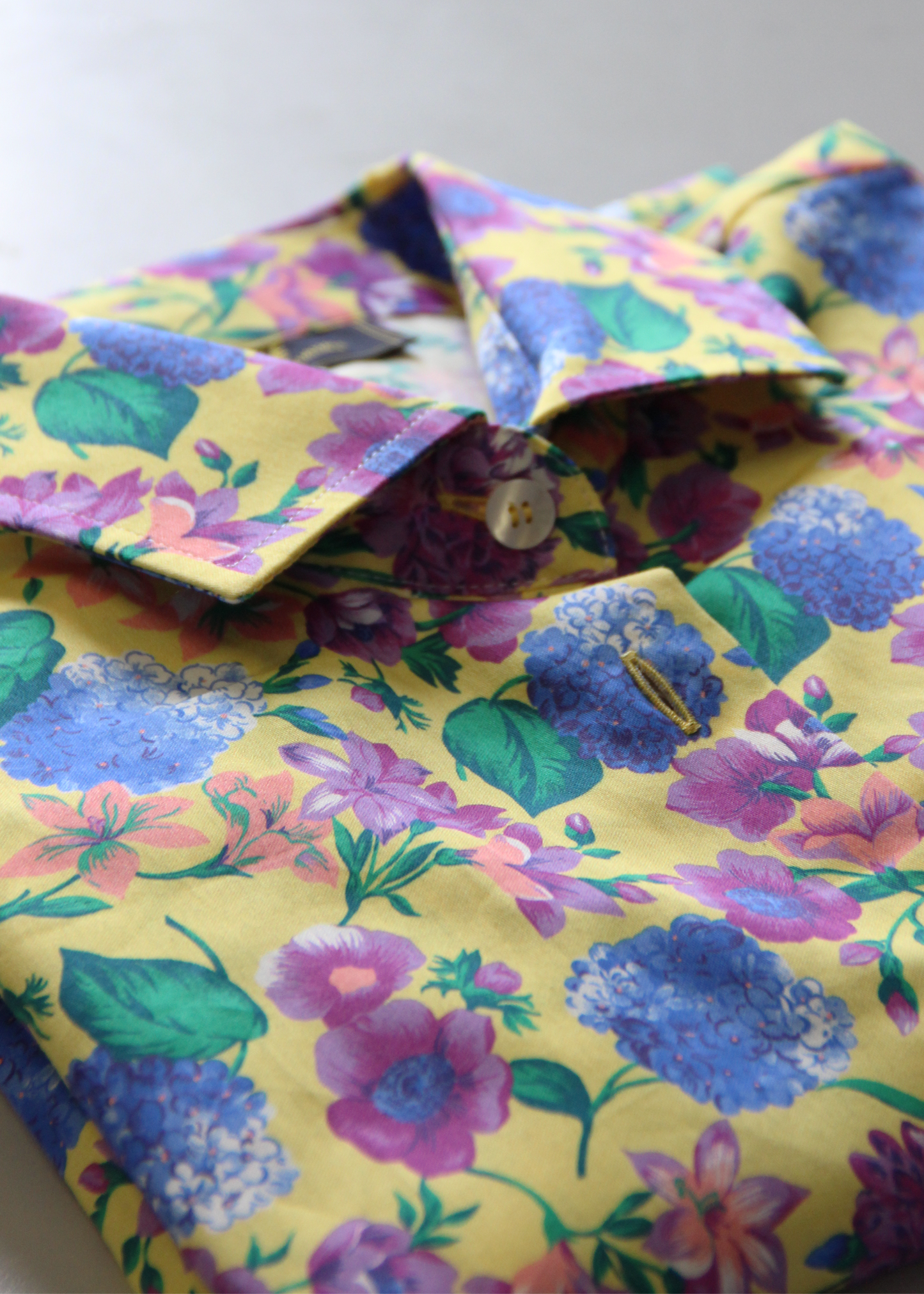 Camicia da donna in cotone dal taglio classico, realizzata artigianalmente da Strike Inside. Il tessuto leggero e traspirante presenta una vivace fantasia floreale con uno sfondo giallo luminoso, arricchito da eleganti fiori nei toni del viola e del blu. Il design con colletto tradizionale e chiusura con bottoni la rende perfetta per un look sia casual che raffinato. Un capo unico che unisce artigianalità e stile, ideale per aggiungere un tocco di colore e femminilità al guardaroba.