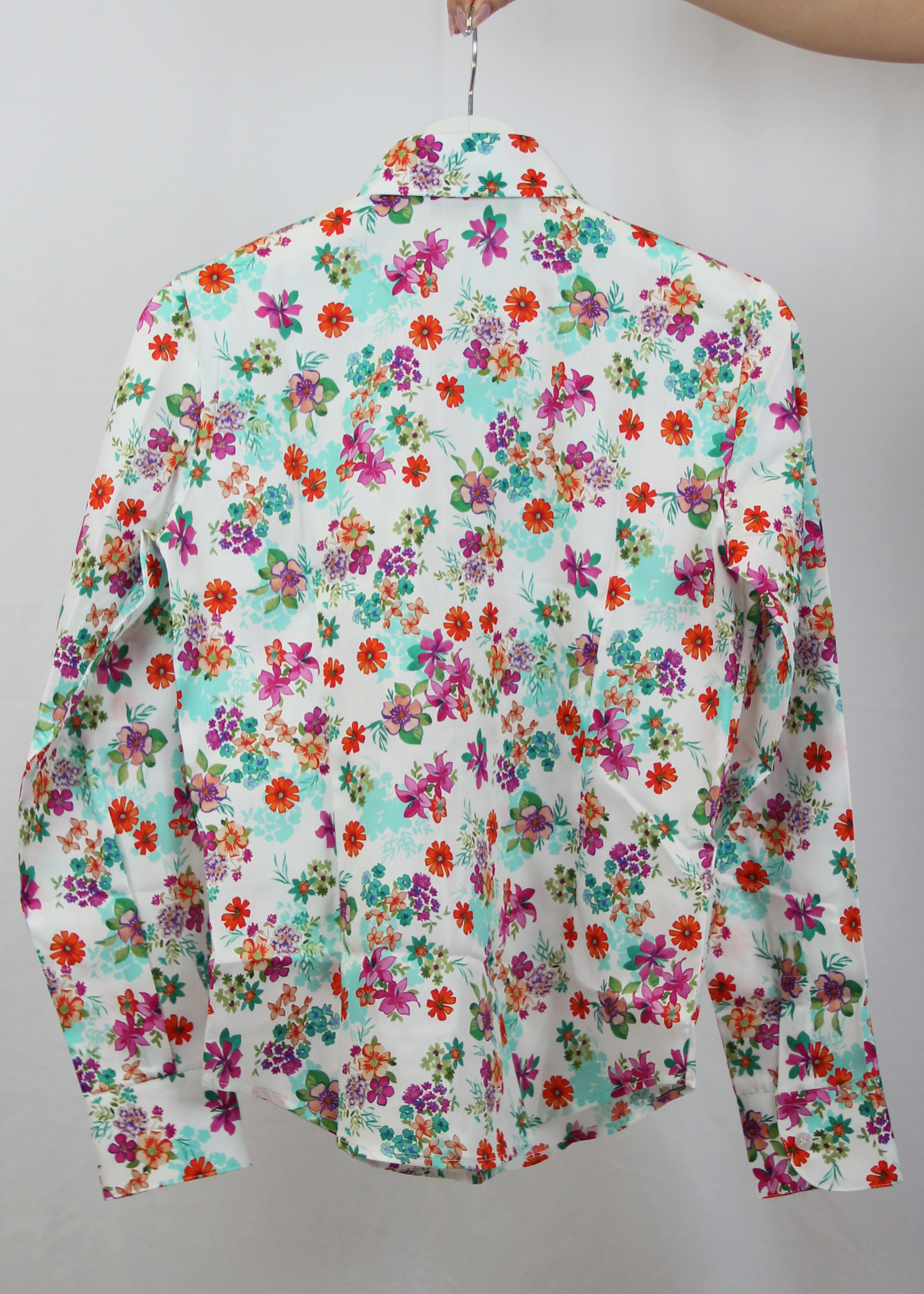 Camicia da donna in cotone dal taglio classico, realizzata artigianalmente da Strike Inside. Il tessuto leggero e traspirante presenta una vivace fantasia floreale su sfondo bianco, decorato con fiori multicolore nei toni del rosso, fucsia, verde e viola. Il design con colletto tradizionale e chiusura con bottoni la rende un capo versatile, perfetto per un look fresco e raffinato. Un'elegante espressione di artigianalità e stile, ideale per aggiungere un tocco di colore al guardaroba.