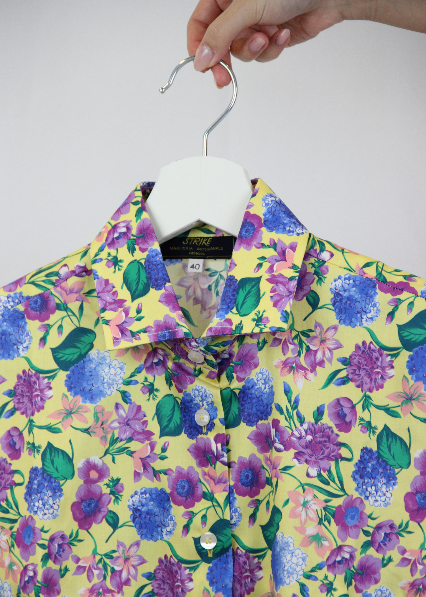 Camicia da donna in cotone dal taglio classico, realizzata artigianalmente da Strike Inside. Il tessuto leggero e traspirante presenta una vivace fantasia floreale con uno sfondo giallo luminoso, arricchito da eleganti fiori nei toni del viola e del blu. Il design con colletto tradizionale e chiusura con bottoni la rende perfetta per un look sia casual che raffinato. Un capo unico che unisce artigianalità e stile, ideale per aggiungere un tocco di colore e femminilità al guardaroba.